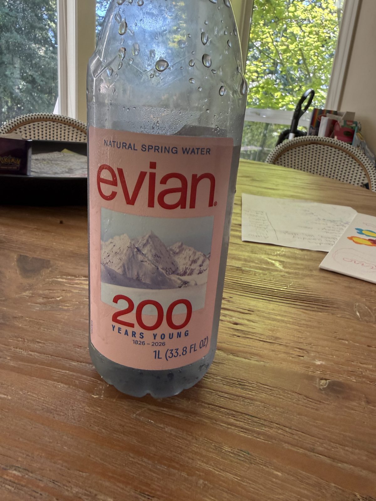 A litre bottle of evian on a wooden table in front of a window, its pink anniversary label reading 200.
